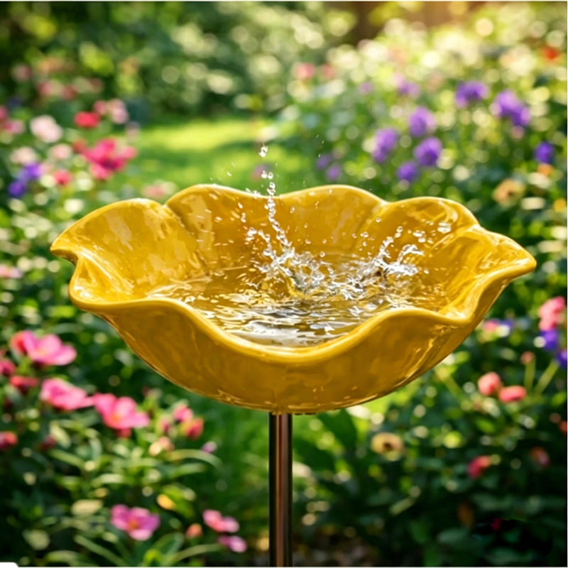 Yellow ceramic bird bath with water splashing in a garden setting